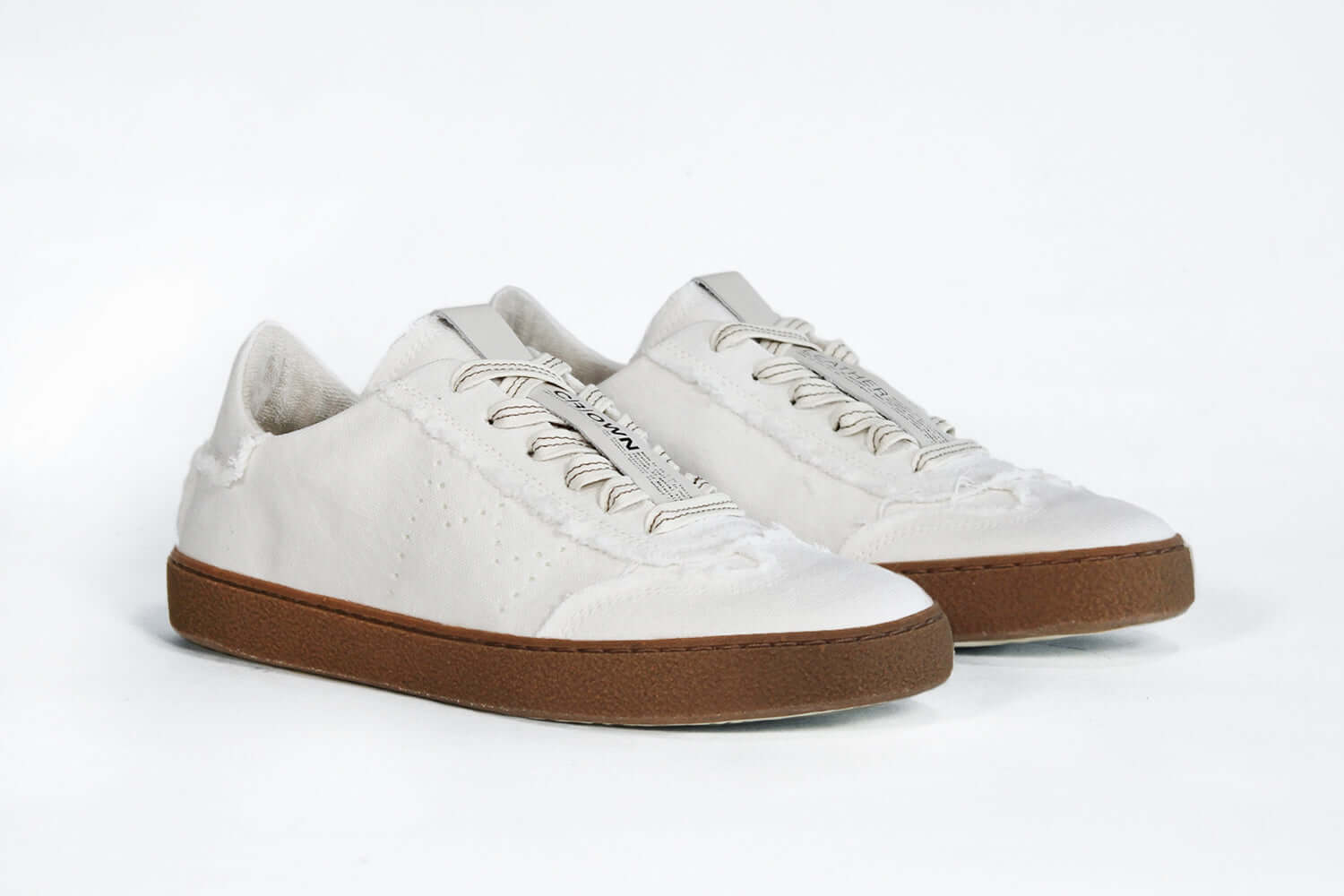 Three quarter front view of low top retro sneaker in distressed white canvas, with honey coloured recycled rubber sole.
