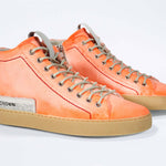 Three quarter front view of high top canvas sneaker. Canvas upper hand painted in gradated fluo orange paint. Pale natural rubber sole.