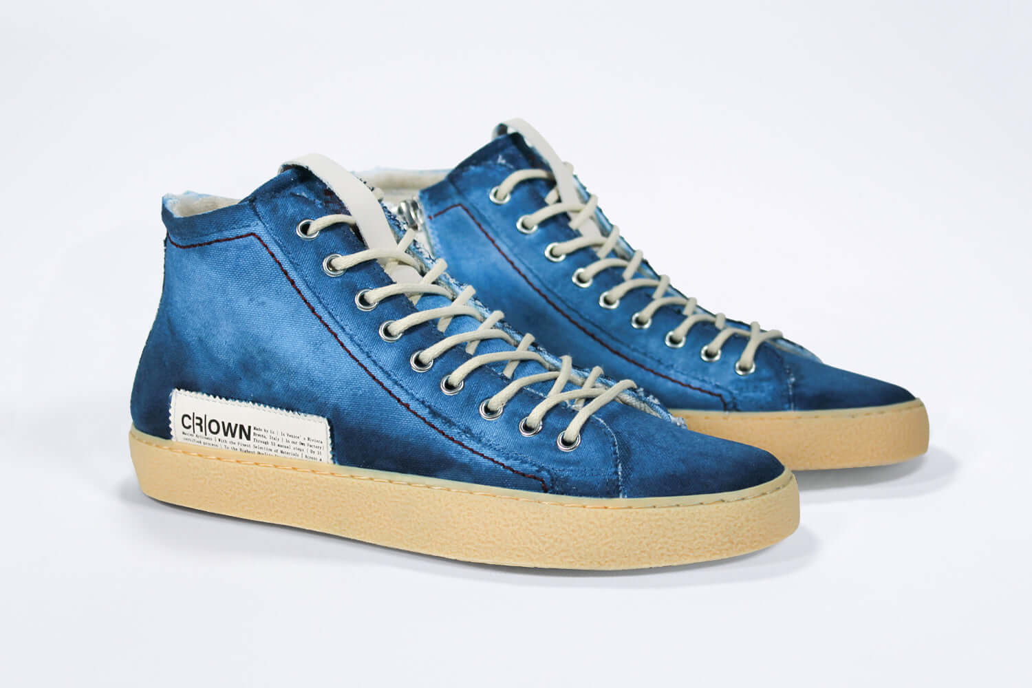 Three quarter front view of high top canvas sneaker. Canvas upper hand painted in gradated blue paint. Pale natural rubber sole.