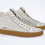 Three quarter front view of high top perforated aged white leather sneaker with signature red stitching and a dark natural rubber sole.