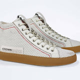 Three quarter front view of high top perforated aged white leather sneaker with signature red stitching and a dark natural rubber sole.