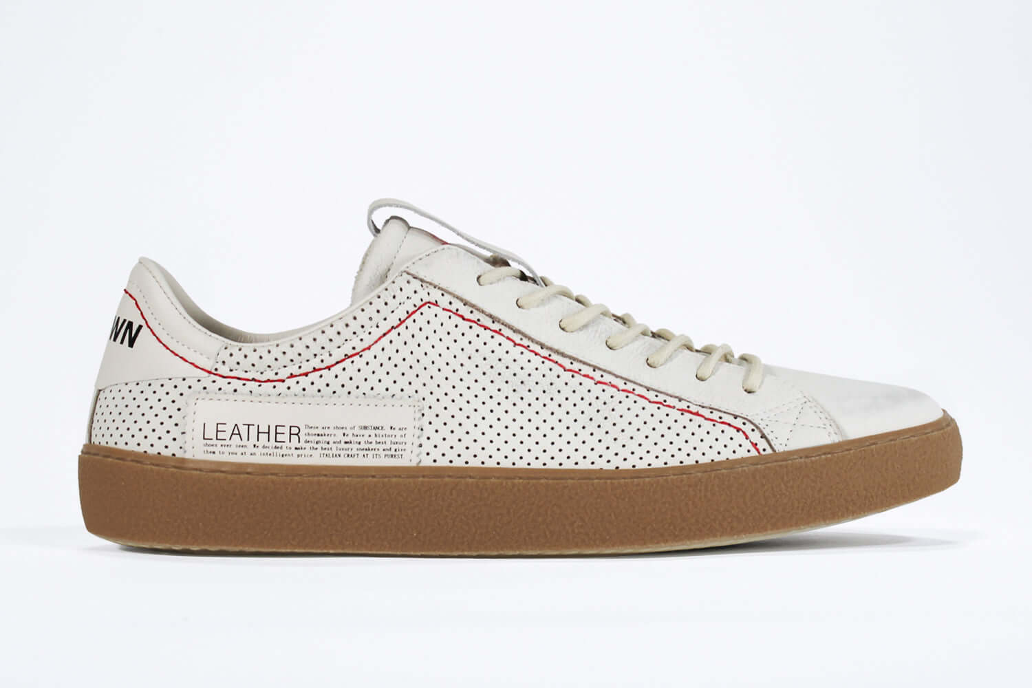 Side profile of low top white sneaker. Perforated aged white leather upper with red stitching and dark rubber sole.