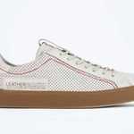 Side profile of low top white sneaker. Perforated aged white leather upper with red stitching and dark rubber sole.