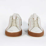 Front view of low top white sneaker. Perforated aged white leather upper with red stitching and dark rubber sole.