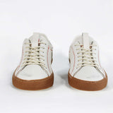 Front view of low top white sneaker. Perforated aged white leather upper with red stitching and dark rubber sole.