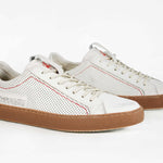 Three quarter front view of low top white sneaker. Perforated aged white leather upper with red stitching and dark rubber sole.