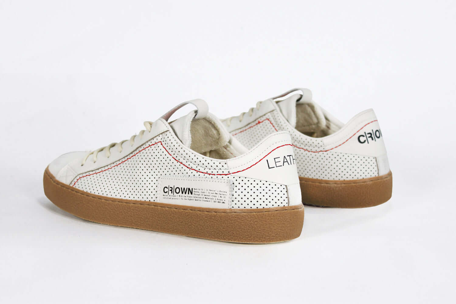 Back view of low top white sneaker. Perforated aged white leather upper with red stitching and dark rubber sole.