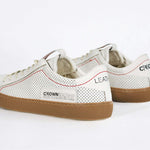 Back view of low top white sneaker. Perforated aged white leather upper with red stitching and dark rubber sole.