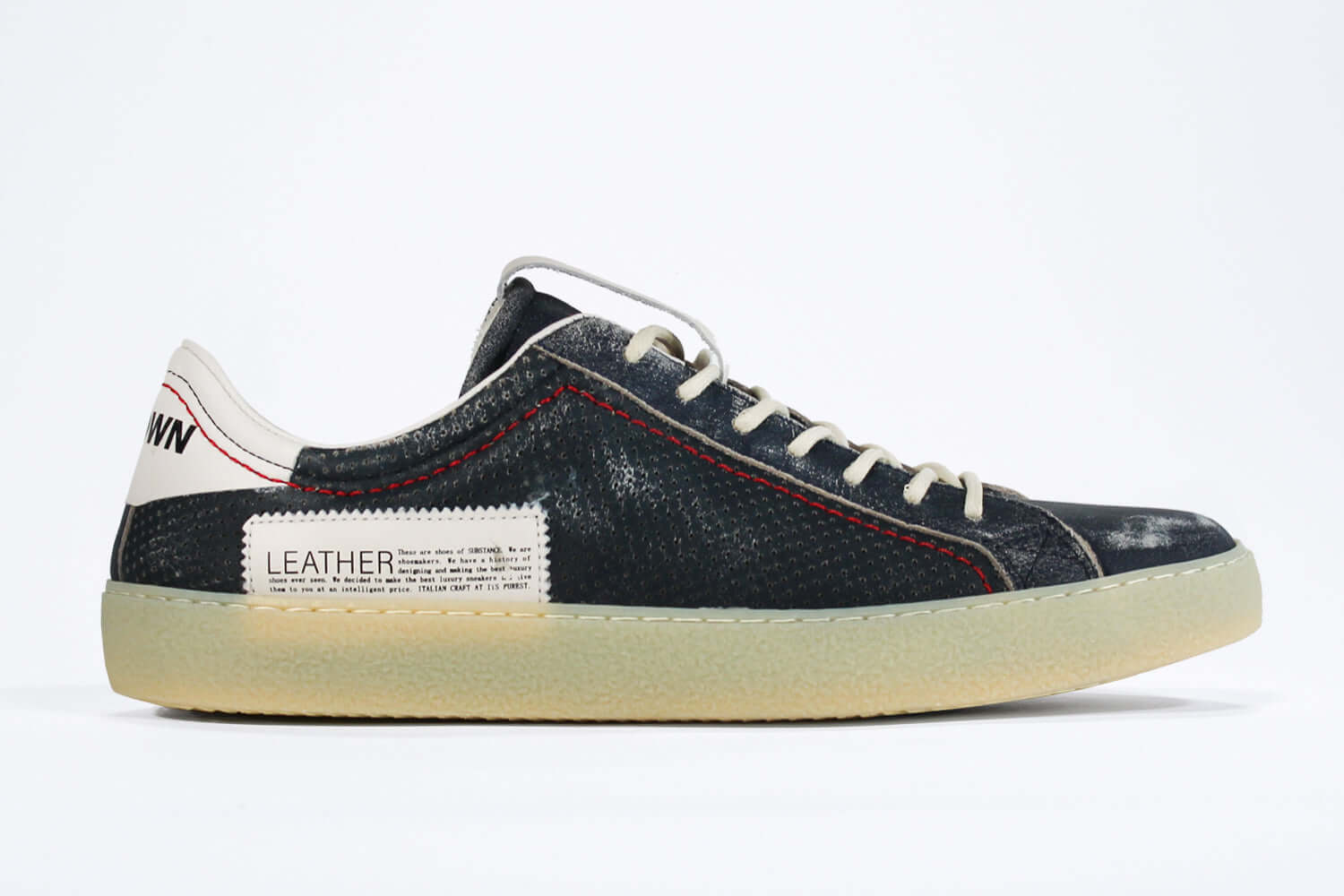 Side profile of low top aged navy sneaker with white accents. Perforated navy leather upper with red stitching and pale rubber sole.