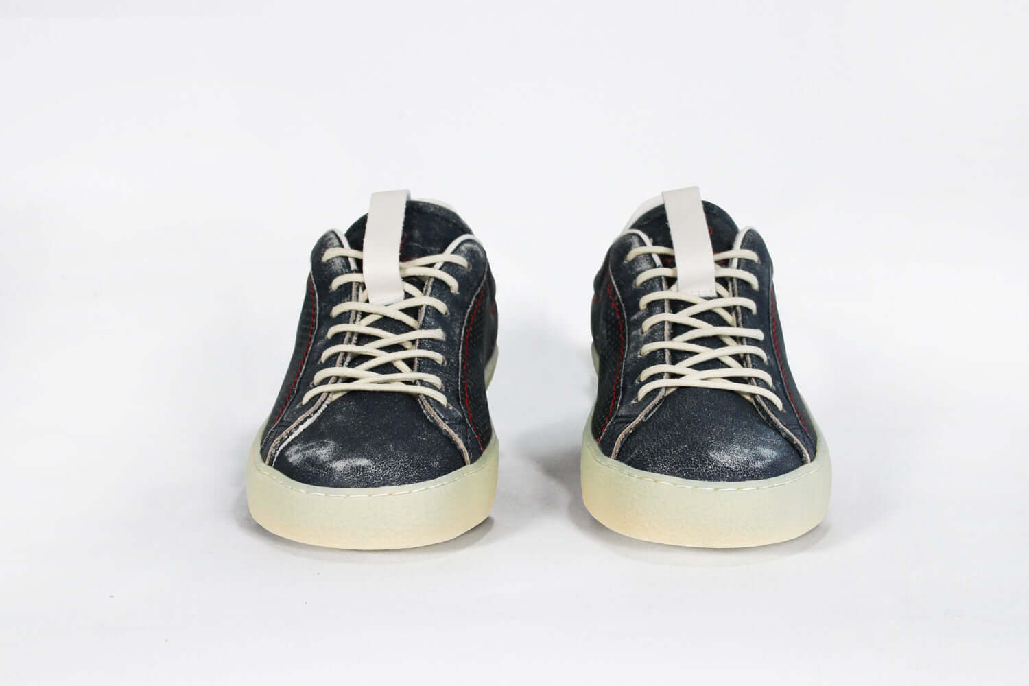 Front view of low top aged navy sneaker with white accents. Perforated navy leather upper with red stitching and pale rubber sole.