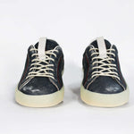 Front view of low top aged navy sneaker with white accents. Perforated navy leather upper with red stitching and pale rubber sole.