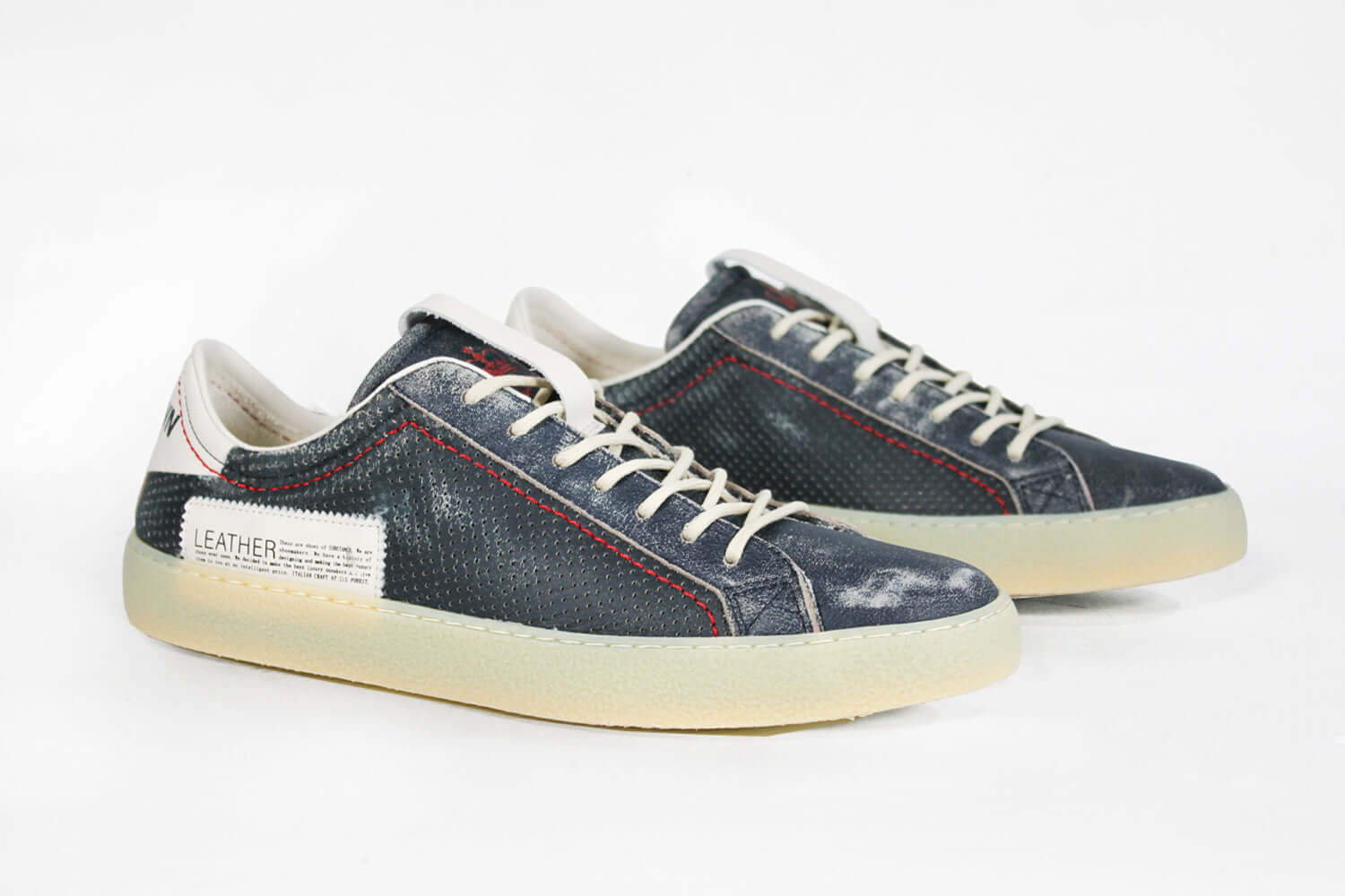 Three quarter front view of low top aged navy sneaker with white accents. Perforated navy leather upper with red stitching and pale rubber sole.