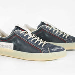 Three quarter front view of low top aged navy sneaker with white accents. Perforated navy leather upper with red stitching and pale rubber sole.