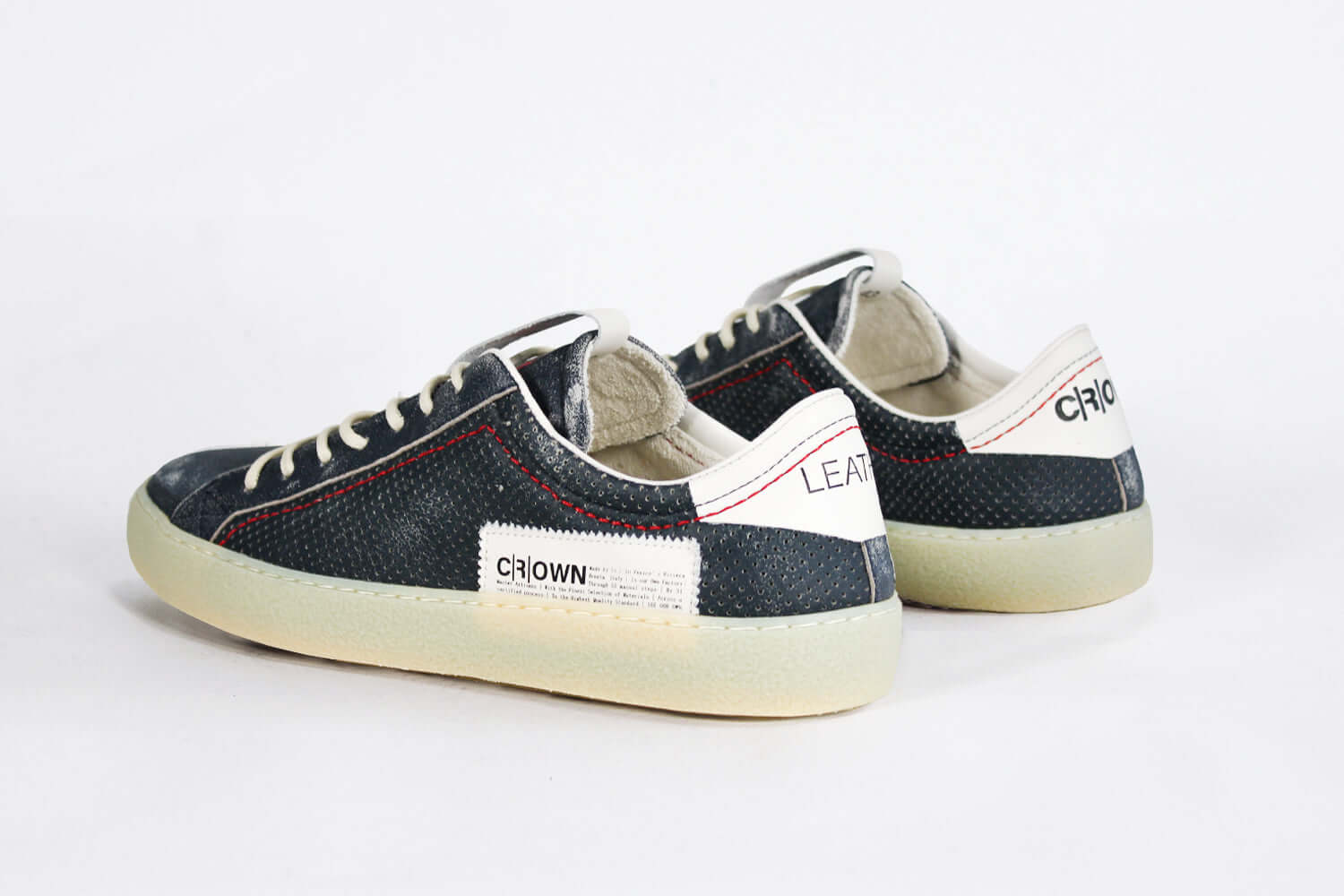 Back view of low top aged navy sneaker with white accents. Perforated navy leather upper with red stitching and pale rubber sole.