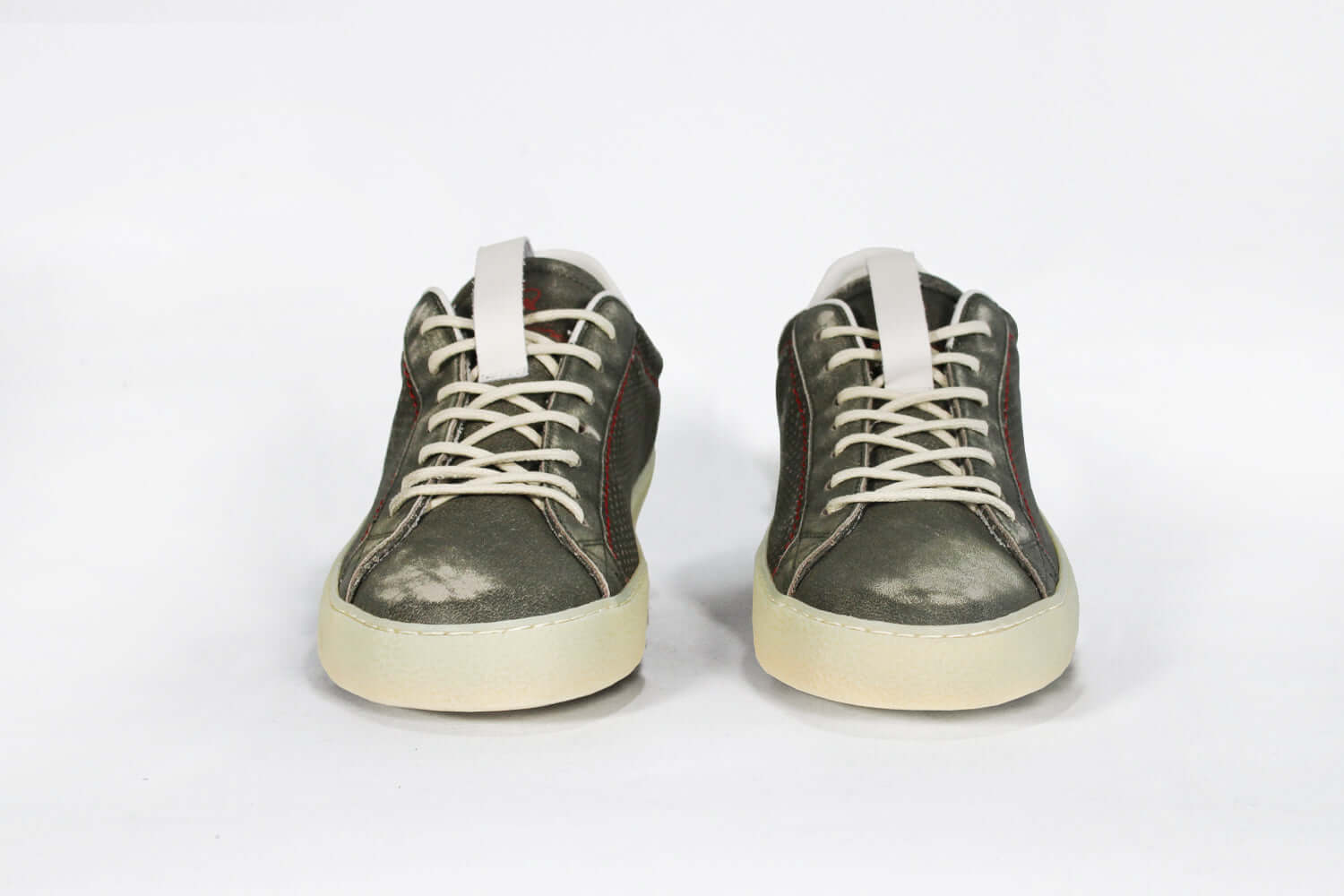 Front view of low top aged khaki sneaker with white accents. Perforated khaki leather upper with red stitching and pale rubber sole.