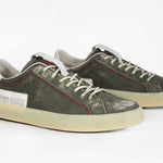 Three quarter front view of low top aged khaki sneaker with white accents. Perforated khaki leather upper with red stitching and pale natural rubber sole.