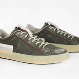 Three quarter front view of low top aged khaki sneaker with white accents. Perforated khaki leather upper with red stitching and pale natural rubber sole.