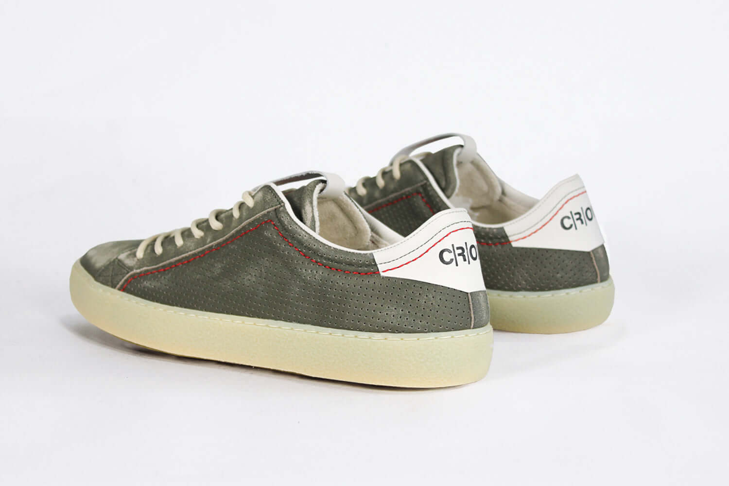Back view of low top aged khaki sneaker with white accents. Perforated khaki leather upper with red stitching and pale rubber sole.