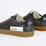 Back view of low top black sneaker. Perforated aged black leather upper with red stitching and dark rubber sole.