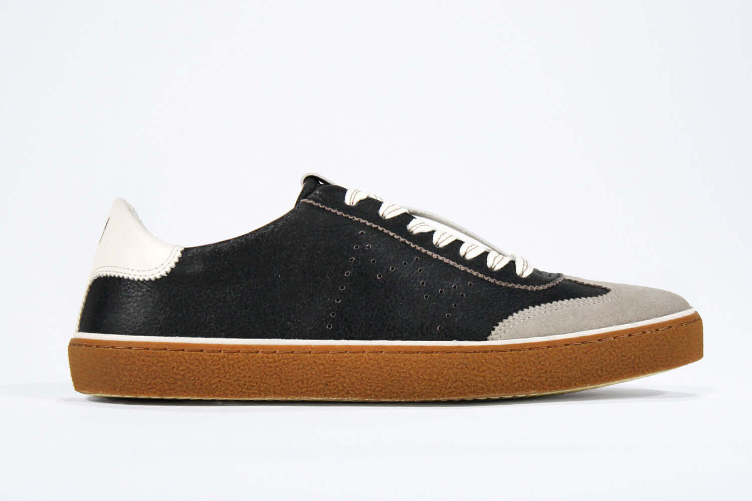 Side view of low top retro sneaker in distressed black leather with white and grey detailing. Set on a honey coloured recycled rubber sole.