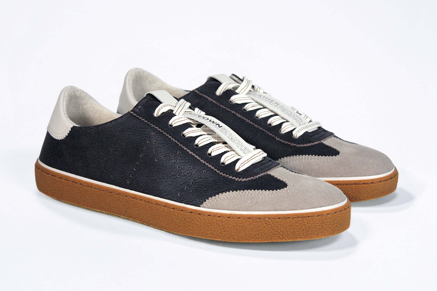 Three quarter front view of low top retro sneaker in distressed black leather with white and grey detailing. Set on a honey coloured recycled rubber sole.