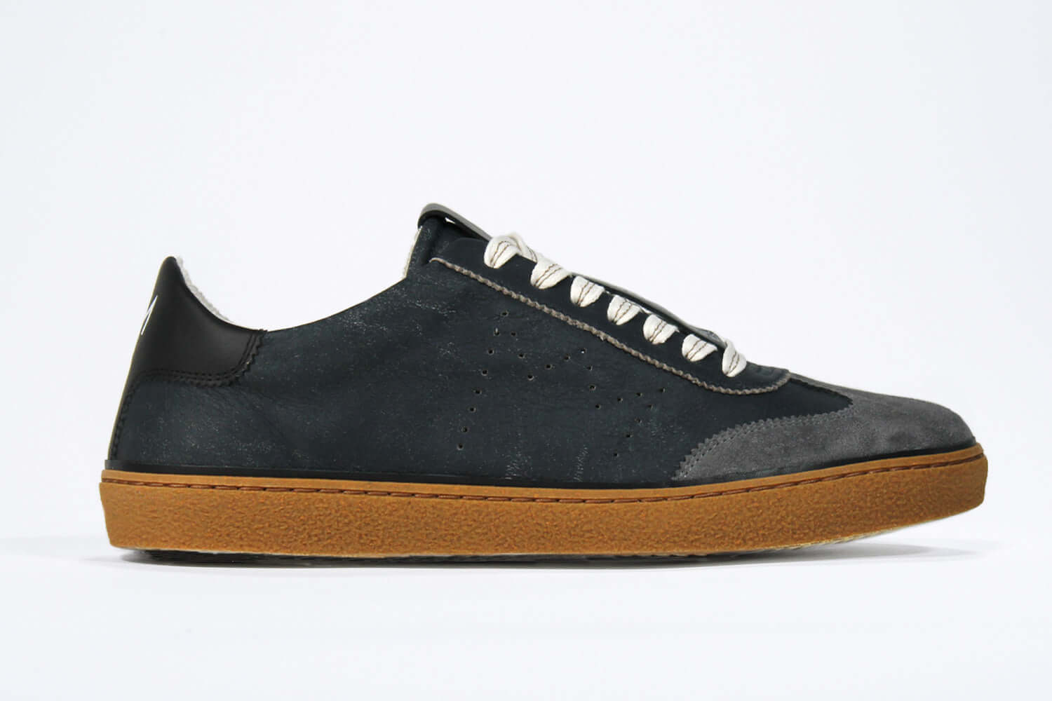 Side view of low top retro sneaker in distressed navy leather with black and grey detailing. Set on a honey coloured recycled rubber sole.