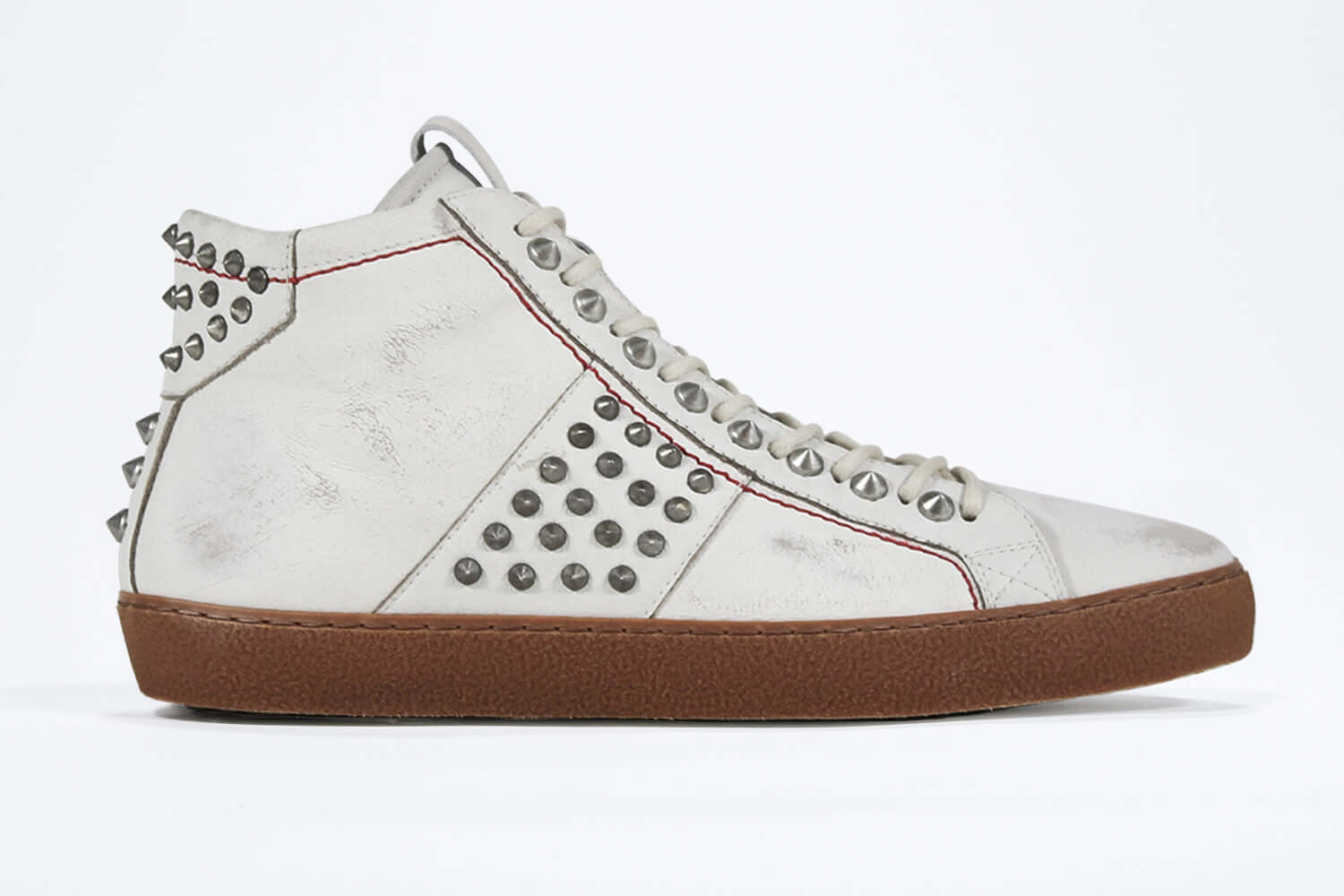 Side profile of mid top aged white sneaker. Full leather upper with silver studs, an internal zip and dark natural rubber sole.