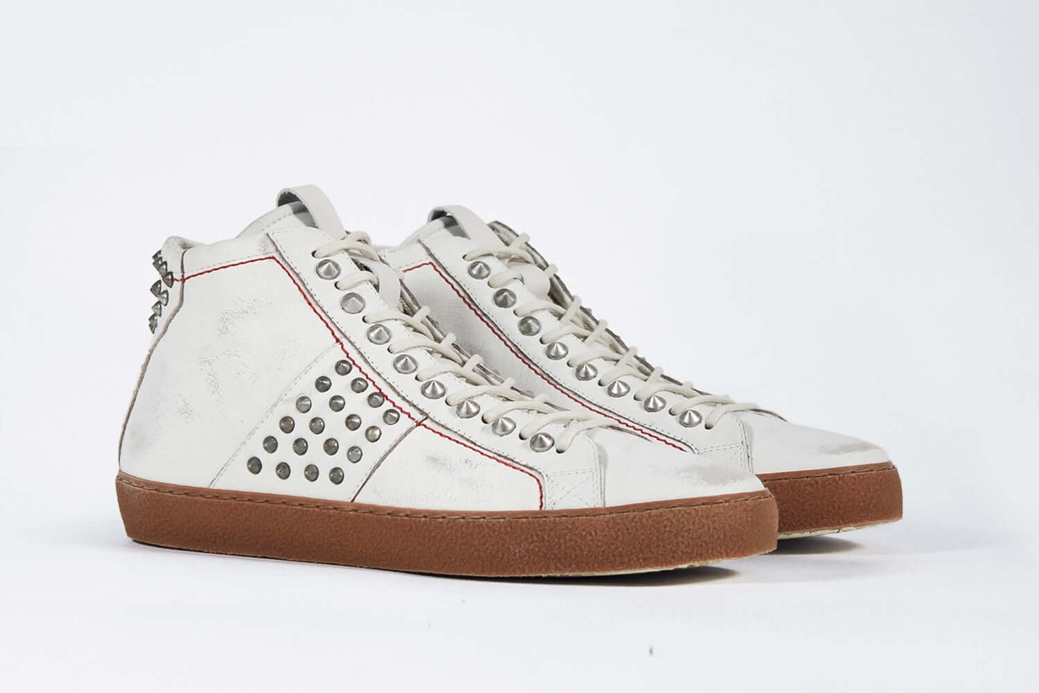 Three quarter front view of mid top aged white sneaker. Full leather upper with silver studs, an internal zip and dark natural rubber sole.