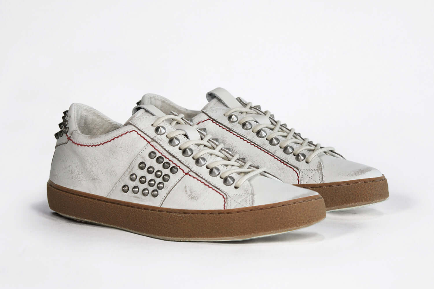 Three quarter front view of low top white studded sneaker. Aged white leather upper with silver studs and dark natural rubber sole.
