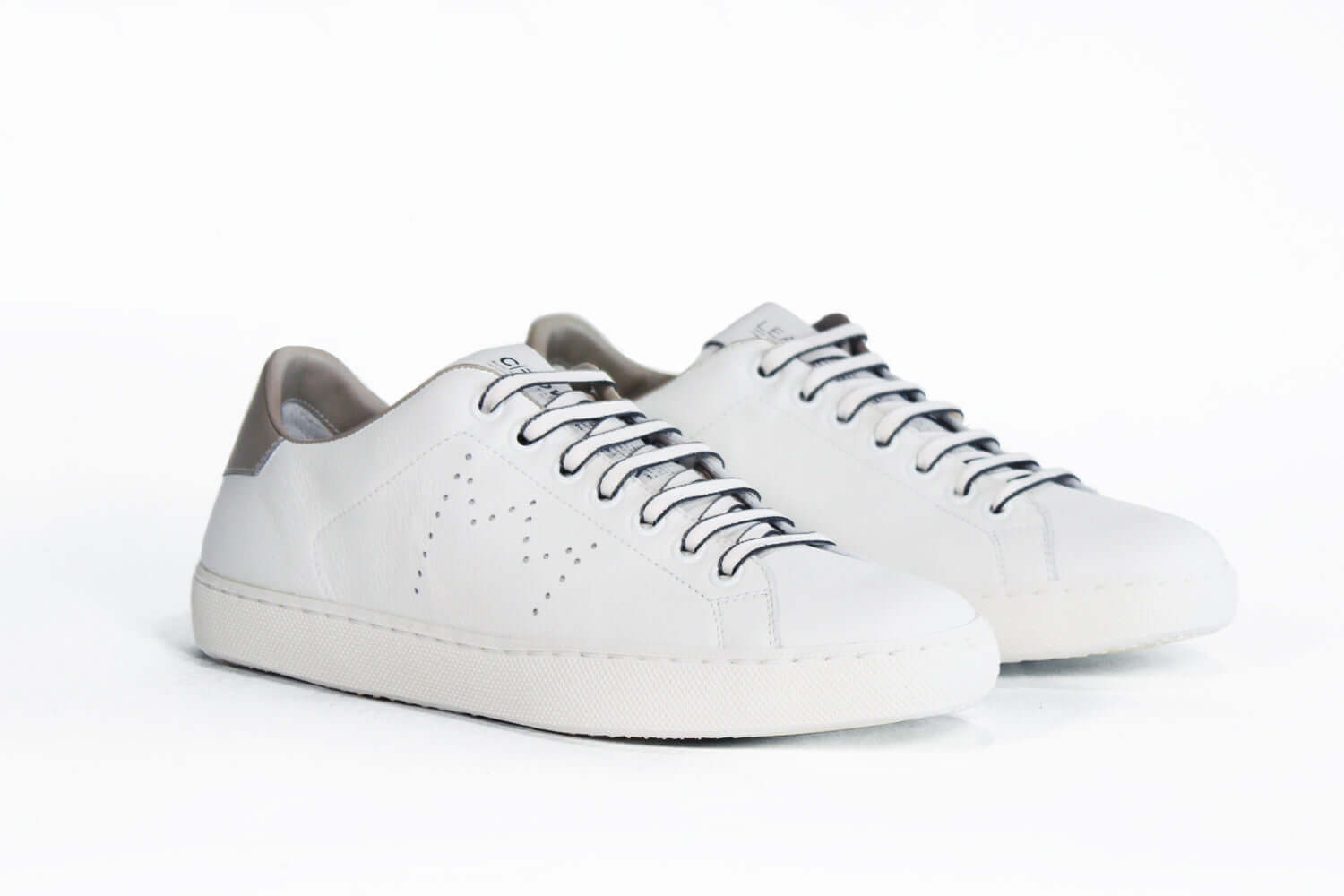 The quarter front view of low top white sneaker with beige detailing and perforated crown logo on upper. Full leather upper and white rubber sole.