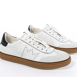 Three quarter front view of low top retro sneaker in white and grey with navy detailing and perforated crown logo on upper. Full leather upper and honey colored recycled rubber sole.