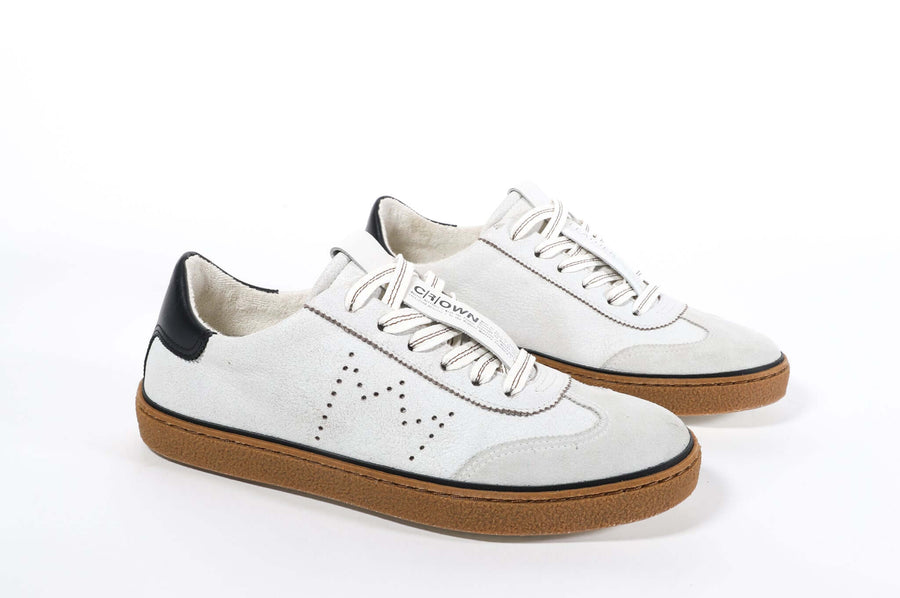 Three quarter front view of low top retro sneaker in white and grey with navy detailing and perforated crown logo on upper. Full leather upper and honey colored recycled rubber sole.