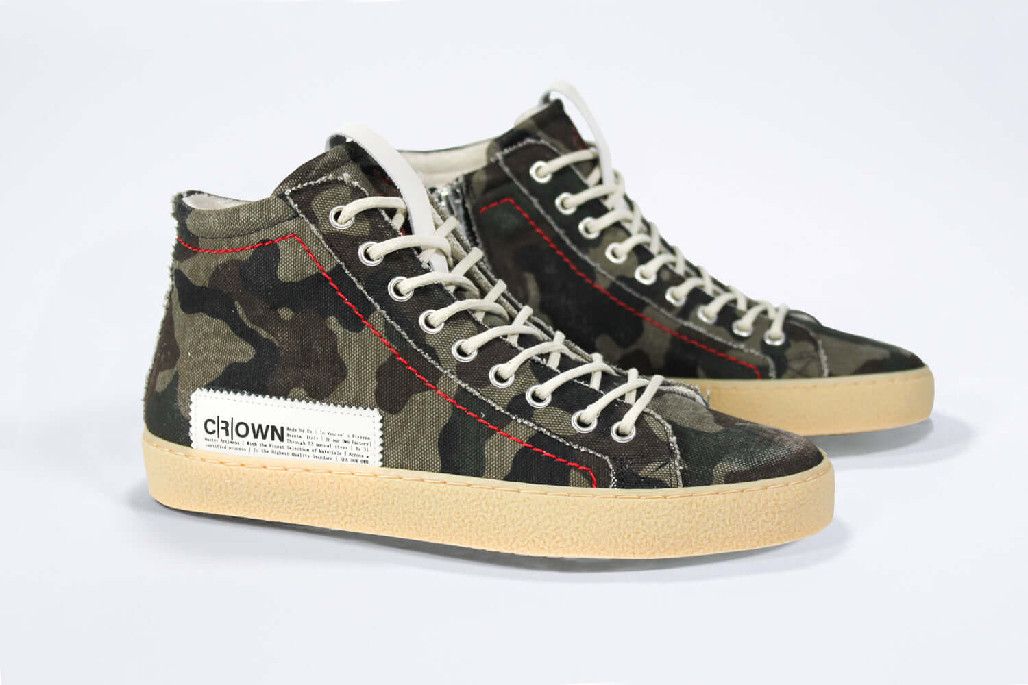 Three quarter front view of high top canvas sneaker. Camouflage print canvas upper with signature red stitching and pale natural rubber sole.