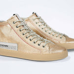 Three quarter front view of high top canvas sneaker. Canvas upper hand painted in gradated gold paint. Natural rubber sole.