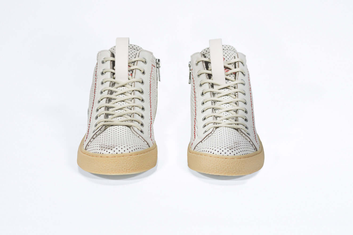 Front view of high top sneaker. Perforated aged white leather sneakers with signature red stitching and pale natural rubber sole.