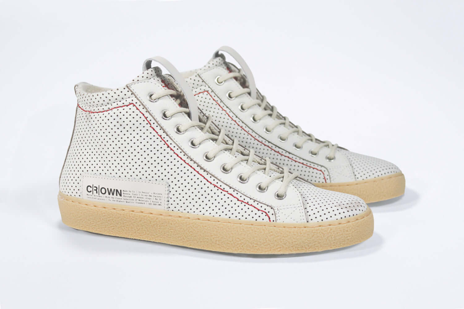 Three quarter front view of high top sneaker. Perforated aged white leather sneakers with signature red stitching and pale natural rubber sole.