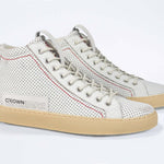 Three quarter front view of high top sneaker. Perforated aged white leather sneakers with signature red stitching and pale natural rubber sole.