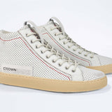 Three quarter front view of high top sneaker. Perforated aged white leather sneakers with signature red stitching and pale natural rubber sole.