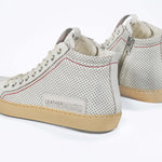 Back view of high top sneaker. Perforated aged white leather sneakers with signature red stitching and pale natural rubber sole.