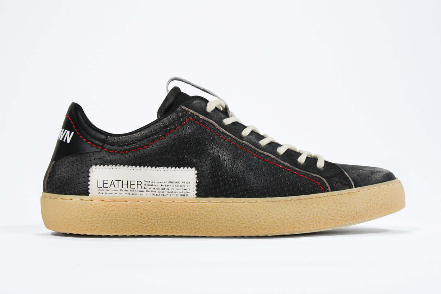Side profile of low top perforated aged black leather sneaker with red stitching detail and a pale natural rubber sole.