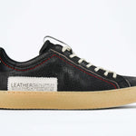Side profile of low top perforated aged black leather sneaker with red stitching detail and a pale natural rubber sole.