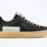 Side profile of low top perforated aged black leather sneaker with red stitching detail and a pale natural rubber sole.