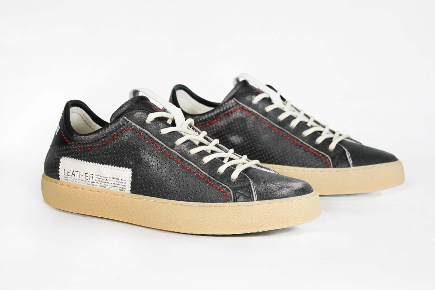 Three  quarter front view of low top perforated aged black leather sneaker with red stitching detail and a pale natural rubber sole.