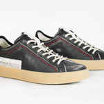 Three  quarter front view of low top perforated aged black leather sneaker with red stitching detail and a pale natural rubber sole.