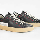 Three  quarter front view of low top perforated aged black leather sneaker with red stitching detail and a pale natural rubber sole.