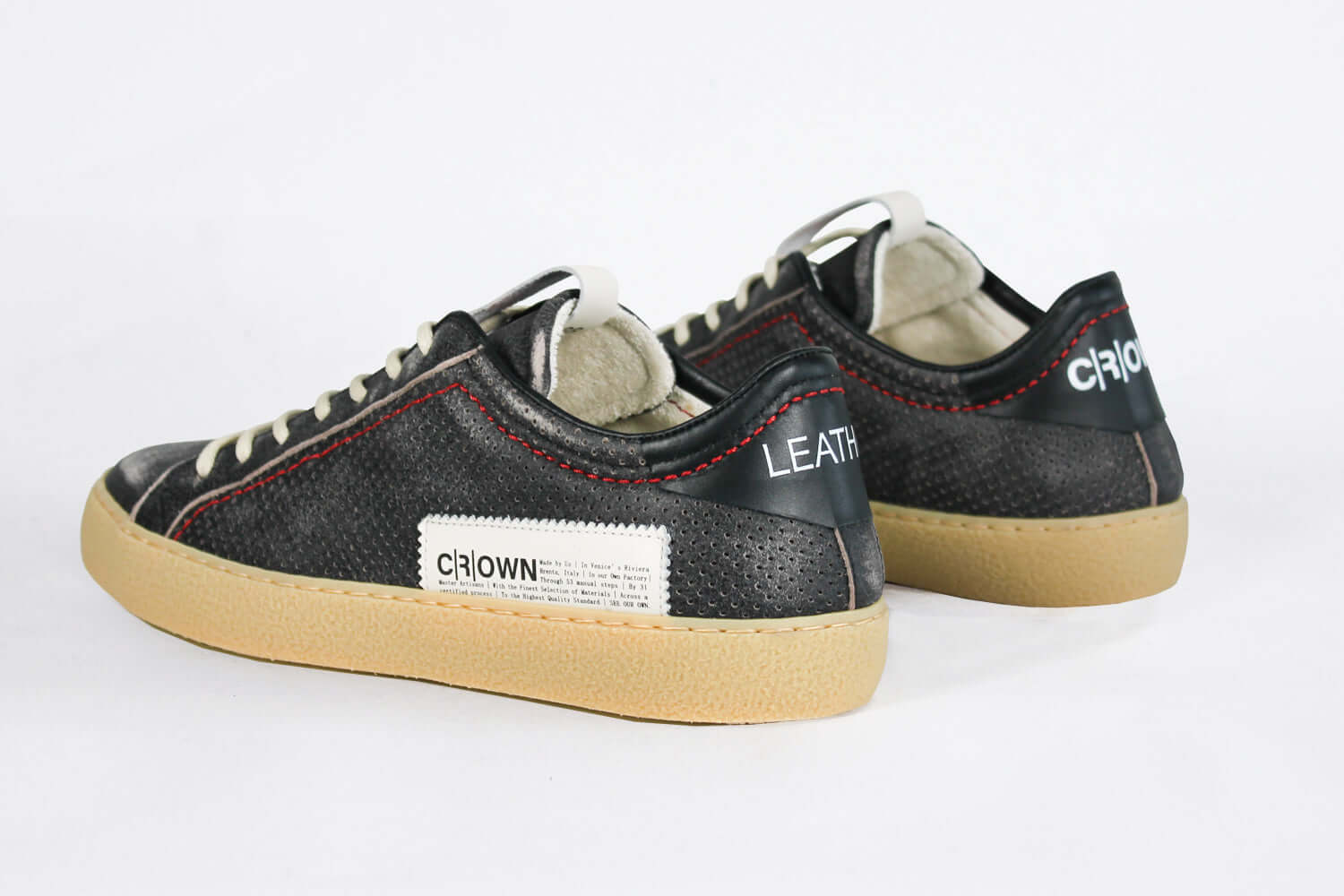 Back view of low top perforated aged black leather sneaker with red stitching detail and a pale natural rubber sole.