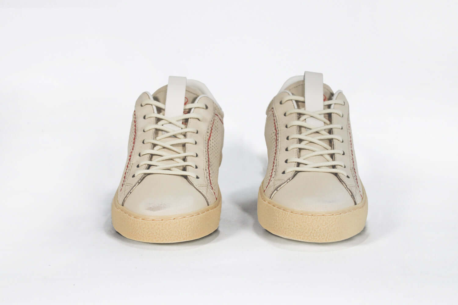 Front view of low top sneaker. Perforated milk leather sneakers with signature red stitching and pale natural rubber sole.