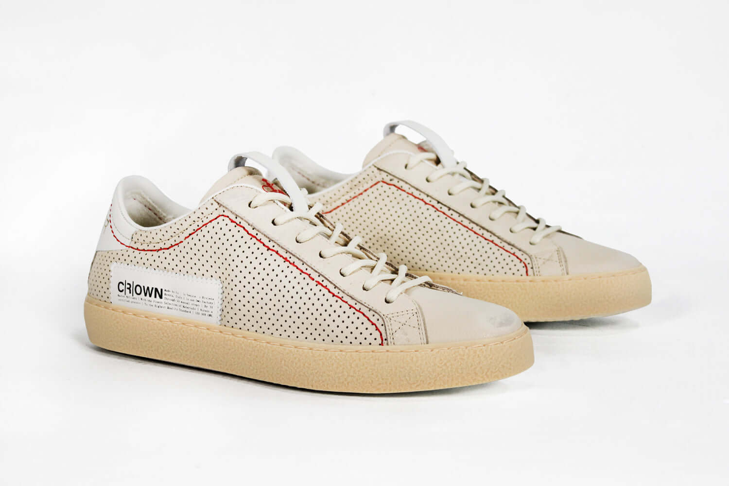 Three quarter front view of low top sneaker. Perforated milk leather sneakers with signature red stitching and pale natural rubber sole.