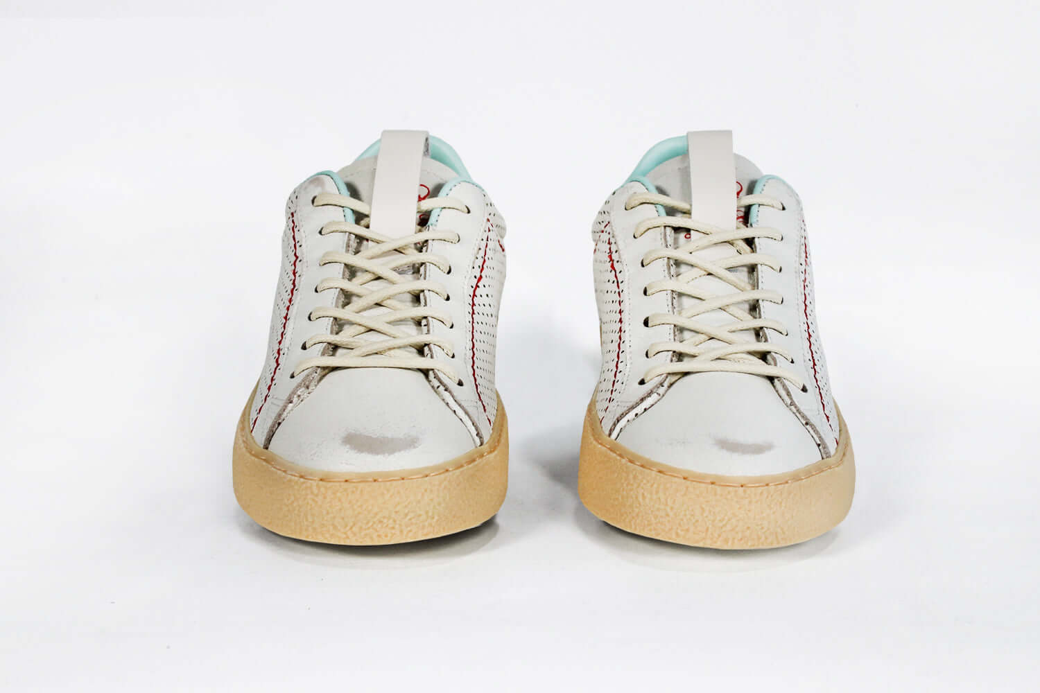 Front view of low top perforated aged white leather sneaker with pale blue accents, red stitching detail and pale rubber sole.