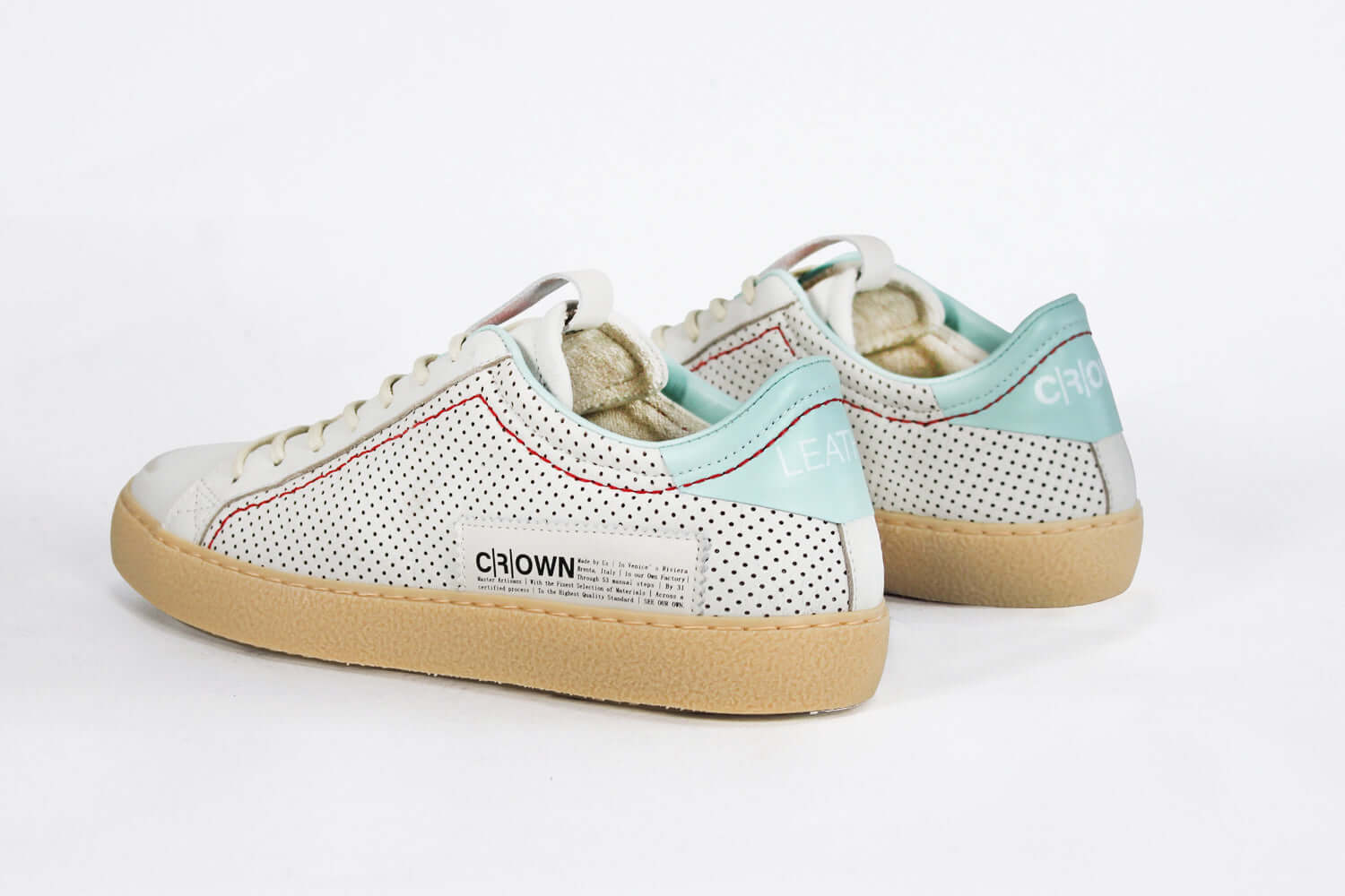Back view of low top perforated aged white leather sneaker with pale blue accents, red stitching detail and pale rubber sole.